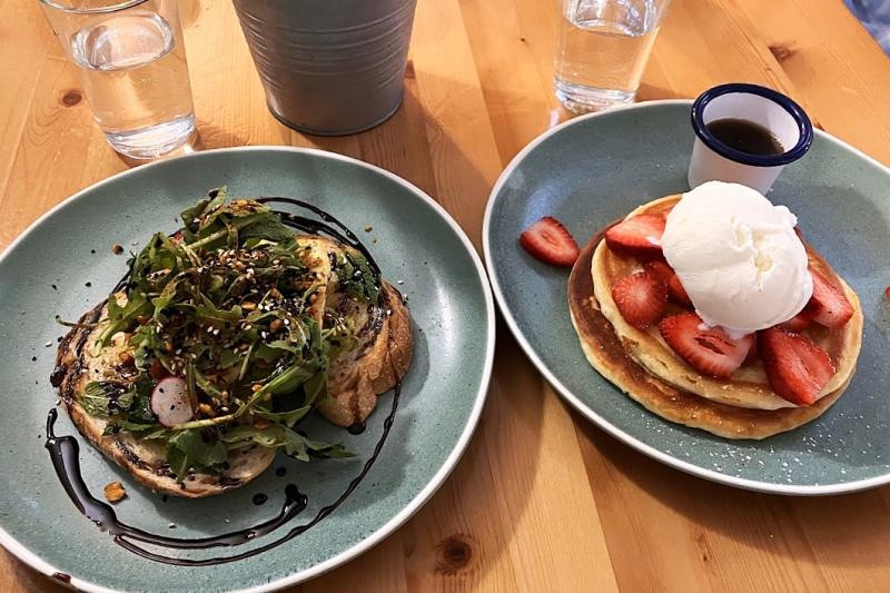 朝食は徒歩すぐのカフェで。スマッシュしたアボカド（熟したアボカドを粗く潰して味付けしたもの）とハルミという焼いても溶けないチーズがのったトースト、ストロベリーパンケーキです。