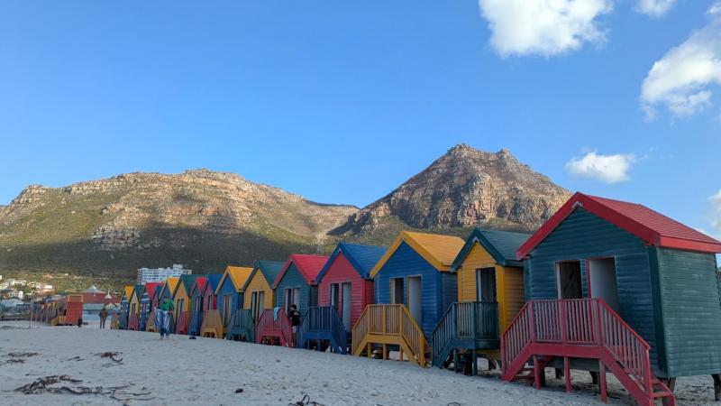 青空と山々を背景に、カラフルなビーチハウスが映えます