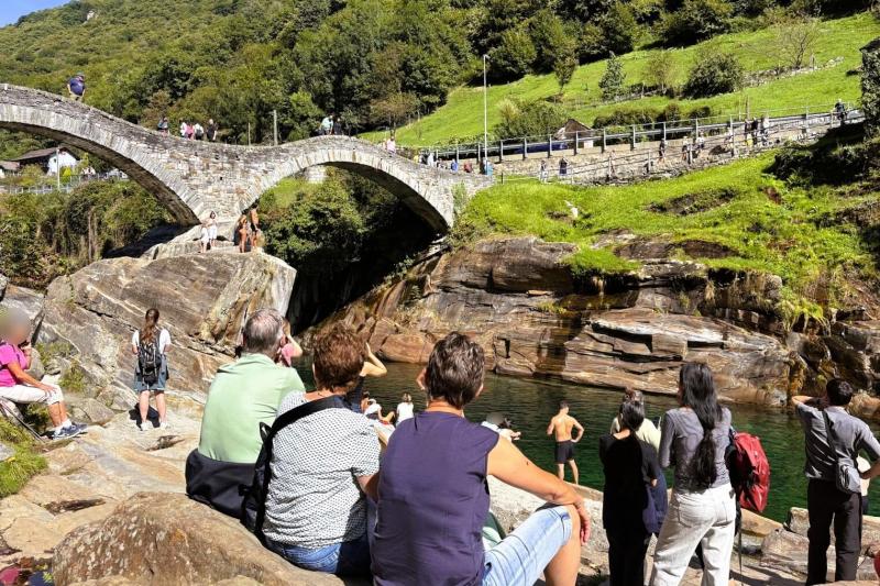 岩の上から川に飛び込む若者を見物する人々