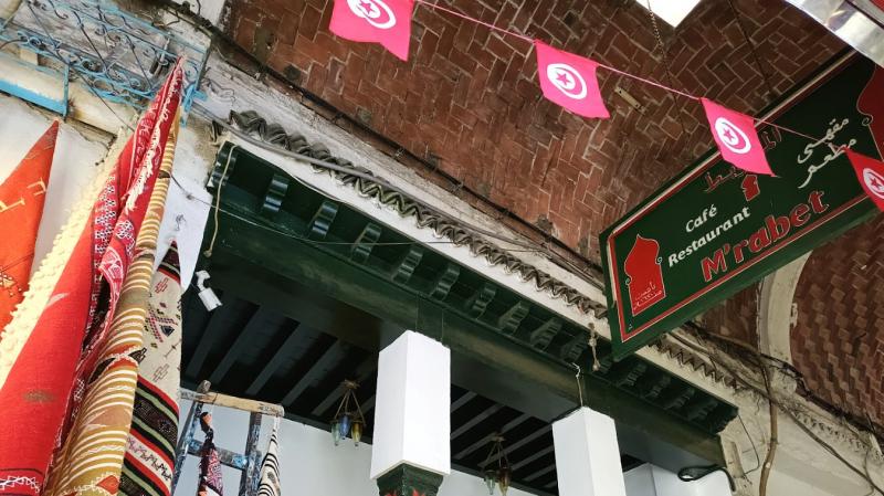 カラフルな絨毯（じゅうたん）や民芸品のお店とチュニジアの赤い国旗が素敵な旧市街